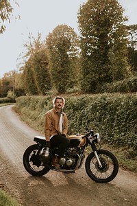 Handsome hipster man sitting on a retro motorcycle in the countryside