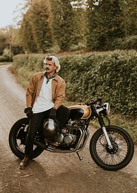 Handsome hipster man sitting on a retro motorcycle in the countryside