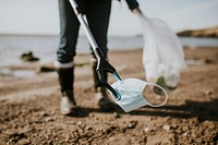 Beach cleanup volunteer picking up face mask for environment campaign