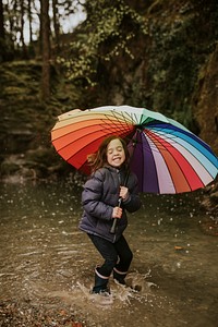 Happy girl playing by the forest lake with an umbrella on a rainy day