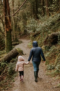 Mother walking with her daughter in the forest rear view