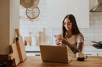 Tattooed woman using her phone and laptop at home