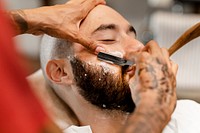 Customer getting a beard trim in a barber shop, small business