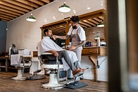 Hairdresser trimming beard of the customer at a barbershop, small business