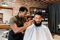 Hairdresser trimming beard of the customer at a barbershop, small business