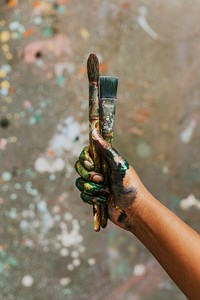 Hands holding paint brush, covered in paint