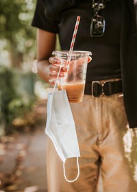 Woman carrying a cup of coffee and a face mask