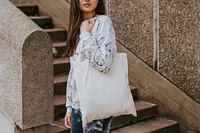 Woman with white tote bag, standing by staircase