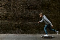 Man skating in town, passing grunge brick wall