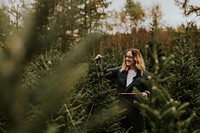 Woman cutting with a bow saw looking for a perfect Christmas tree at a Christmas tree farm