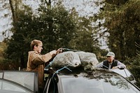 Two men securing his Christmas tree on the car roof