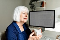 Senior woman holding mug, relaxing in her home office