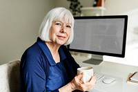 Old woman smiling, holding mug in her home office