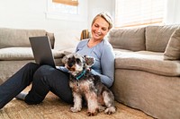 Woman sitting with her dog in the living room, working on laptop