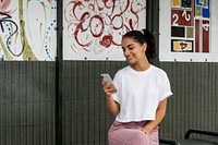 Hispanic woman in white tee texting at bus stop, casual apparel fashion