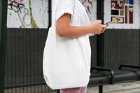 Woman with tote bag, texting on phone at bus stop