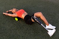 Woman athlete with prosthetic leg resting her back on a back roller