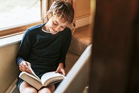 Young boy reading by a window, new normal hobby