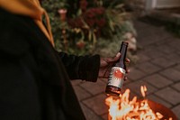 Man carrying a beer bottle by a fireside