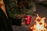 Man carrying a party cup by a fireside