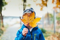 Young boy covering his face with an autumn leaf