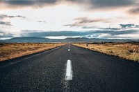 A view from the middle of an asphalt road as it disappears into the horizon. There are mountains in the distance. A metaphor for endless possibilities.