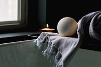 White and yellow bath bomb on wooden tray over tub with towel and lit candle, free public domain CC0 image.