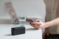 Woman using phone to control portable bluetooth speaker on counter.