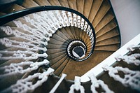 Looking down from the top of an elegant spiral staircase with a black railing and ornate white rungs makes us feel like Alice falling down the rabbit hole.