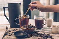 Free woman stirring coffee, cream and sugar containers, roasted coffee beans photo, public domain beverage CC0 image.