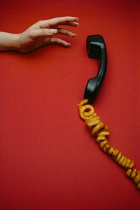 Free woman's hand reaches for a receiver with curly fries as the telephone cord against a red background image, public domain CC0 photo.