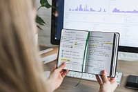 Free woman reading notes from journal in front of computer screen photo, public domain book CC0 image.