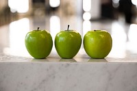 Three green apples on a marble counter top.