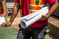 A construction worked hold a roll of blueprints in they arm on a construction site.