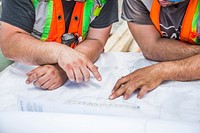 The hands of construction workers going over blueprints on a construction site.