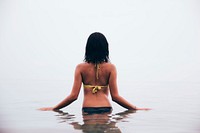 A woman faces away with her hands to the side waste deep in still water with reflection.