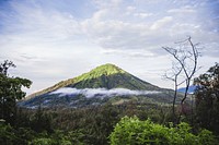 A green mountain peak with wisps of cloud surrounding it.