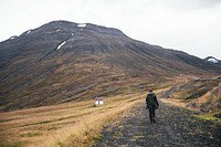 Hiker going through the Icelandic path, next to a white farmhouse.