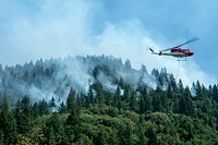 A helicopter scoops up water from the stream to drop onto the forest fires in the Mendocino National Forest, California. (Forest Service photo by Cecilio Ricardo). Original public domain image from <a href="https://www.flickr.com/photos/usforestservice/43439626134/" target="_blank" rel="noopener noreferrer nofollow">Flickr</a>
