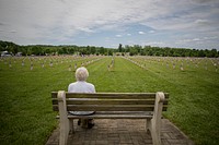 Elderly woman sits on a park bench remembering her husband, a Navy veteran, during a Memorial Day observance. Original public domain image from Flickr