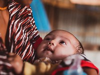 Baby in the arms of a woman. Energi Terbarukan Berikan Manfaat untuk Kehidupan. Photo by: Rwaida Gharib. Original public domain image from Flickr