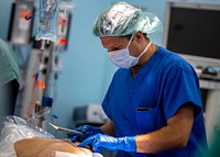 200430-N-PH222-1517 LOS ANGELES (April 30, 2020) Lt. Cmdr. Patrick Morrissey, from San Diego, inspects staples on a patient prior to surgery in an operating room aboard the hospital ship USNS Mercy (T-AH 19).