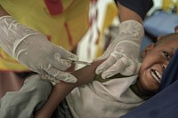 A health worker vaccinates a child at the Maternal and Child Health Centre in Hamar-Jajab district of Mogadishu, Somalia, on 19 September 2020. The Somali federal Ministry of Health, supported by the World Health Organisation (WHO), UNICEF, the Global Polio Eradication Initiative (GPEI), and Gavi, recently concluded a mass measles and polio immunization campaign. Nearly half a million children in Mogadishu and Benadir region can now hope for healthier and productive lives, thanks to the UN-supported immunization exercise. UN Photo/Mukhtar Nuur. Original public domain image from Flickr