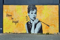 Jacob Root aka Distranged DesignOn the side of the Lemon Tree Cafe, an iconic image of Audrey Hepburn, painted in a grey-scale stencil style against a bright yellow background, painted in Jacob Root's signature style, Christchurch, Canterbury, New Zealand- January 13, 2021. Original public domain image from Flickr