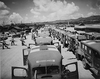 Okinawa Campaign, 1945. Military ambulances lined up on shore at Guam, awaiting the arrival of USS Solace (AH-5) with casualties from Okinawa, 06/04/1945. Among ships in left background is USS LSM-00242, 06/04/1945. Photographer PhoM2c J.G. Mull. Original public domain image from<a href="https://www.flickr.com/photos/navymedicine/51225581820/"> Flickr</a>