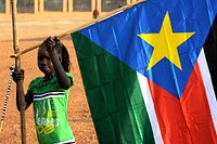 A young girl hangs the South Sudan flag. (Timothy McKulka/USAID). Original public domain image from Flickr