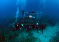From top left, U.S. Navy Chief Explosive Ordnance Disposal Technician Matthew Harrison, Chief Navy Diver Eric Eberle, Navy Diver 3rd Class Brian Stewart, Senior Chief Master Diver Michael Woods, Navy Diver 2nd Class Sean Mcconnell and Chief Warrant Officer John Sullivan, all assigned to Mobile Diving and Salvage Unit 2, Company 4 and the Joint Prisoner of War/Missing In Action (POW/MIA) Accounting Command (JPAC), hold an American flag and a POW/MIA flag Oct. 19, 2012, in Calvi, France, at the site of the wreckage of a B-17 Flying Fortress aircraft that was shot down and sunk during World War II. The team was deployed alongside JPAC aboard salvage ship USNS Grapple (T-ARS-53) as part of a 30-day underwater recovery mission for an unaccounted-for U.S. Service member who went missing during the crash.
