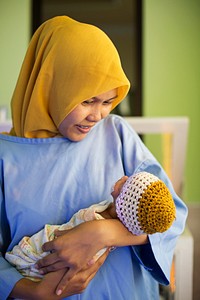 Woman holding baby. Meningkatkan kesehatan ibu dan bayi baru lahir. Restiana menerapkan Perawatan Metode Kangguru pada bayinya, Edgar, di fasilitas kesehatan yang mendapatkan dukungan dari program USAID EMAS. Photo by Syane Luntungan/USAID EMAS. Original public domain image from Flickr