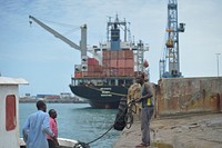 A Somali man helps dock a smaller boat in Mogadishu's port on September 17, 2005, while a much larger container ship gets off loaded in the background. AMISOM Photo / Tobin Jones. Original public domain image from Flickr
