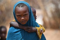 A girl carries her brother at an Internally Displaced Persons camp in Doolow, Gedo region, Somalia on June 12, 2017. A delegation led by the United Nations and the African Union visited the camp during a humanitarian assessment mission to the Horn of Africa region. UN Photo / Ilyas Ahmed. Original public domain image from Flickr